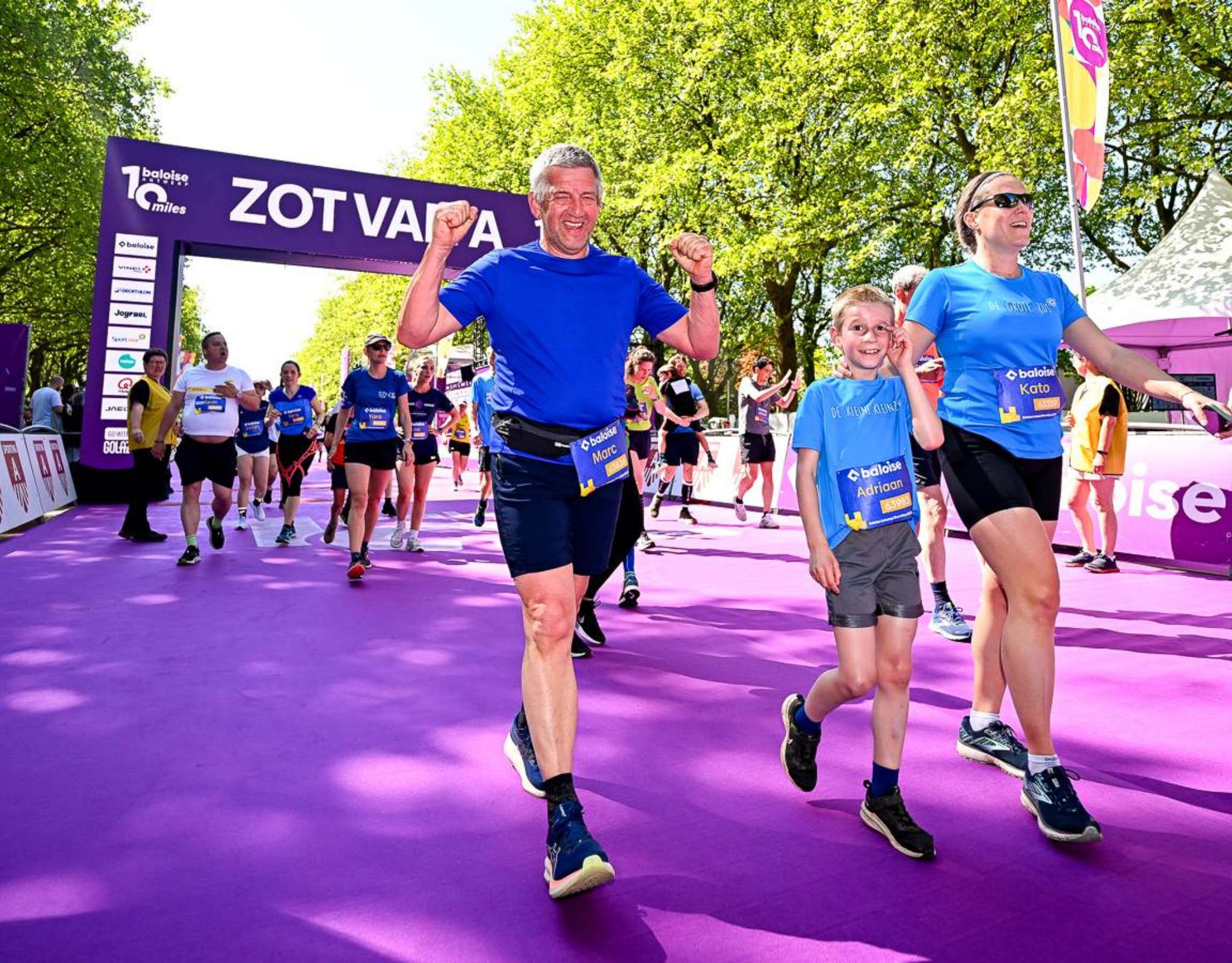 Des participants franchissent la ligne d’arrivée sous l’arche violette « ZOT VAN A 10 miles ».