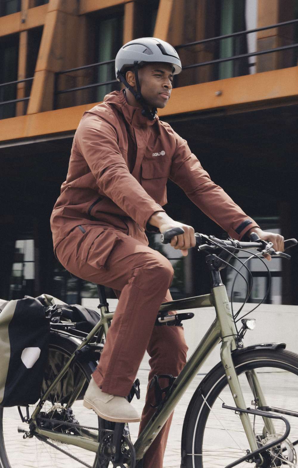 Homme à vélo en ville avec un casque blanc et une tenue de pluie brune