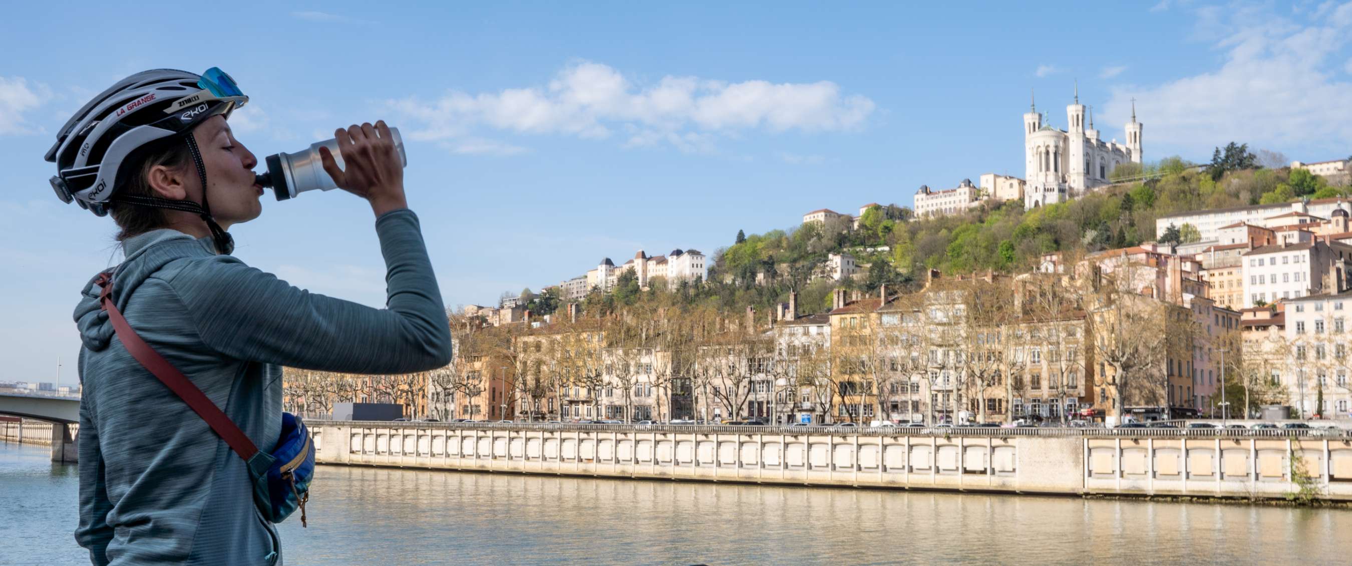 Personne buvant à une gourde au bord de l’eau, avec la ville et la basilique en arrière-plan.