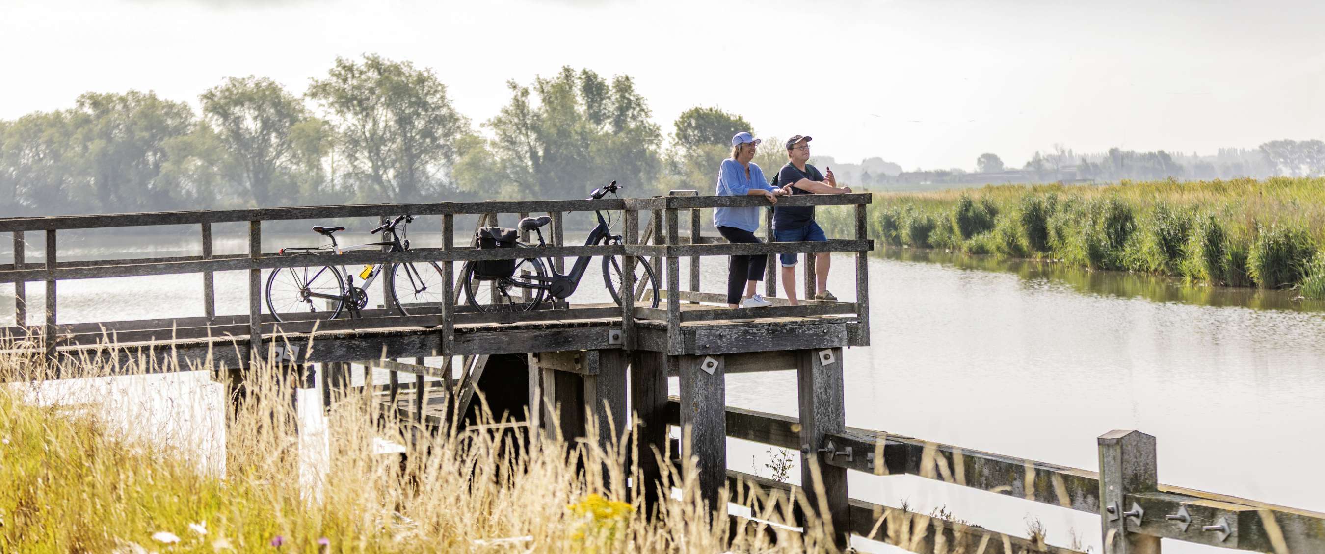 Cyclistes en pause sur une plateforme en bois dans un paysage aquatique.