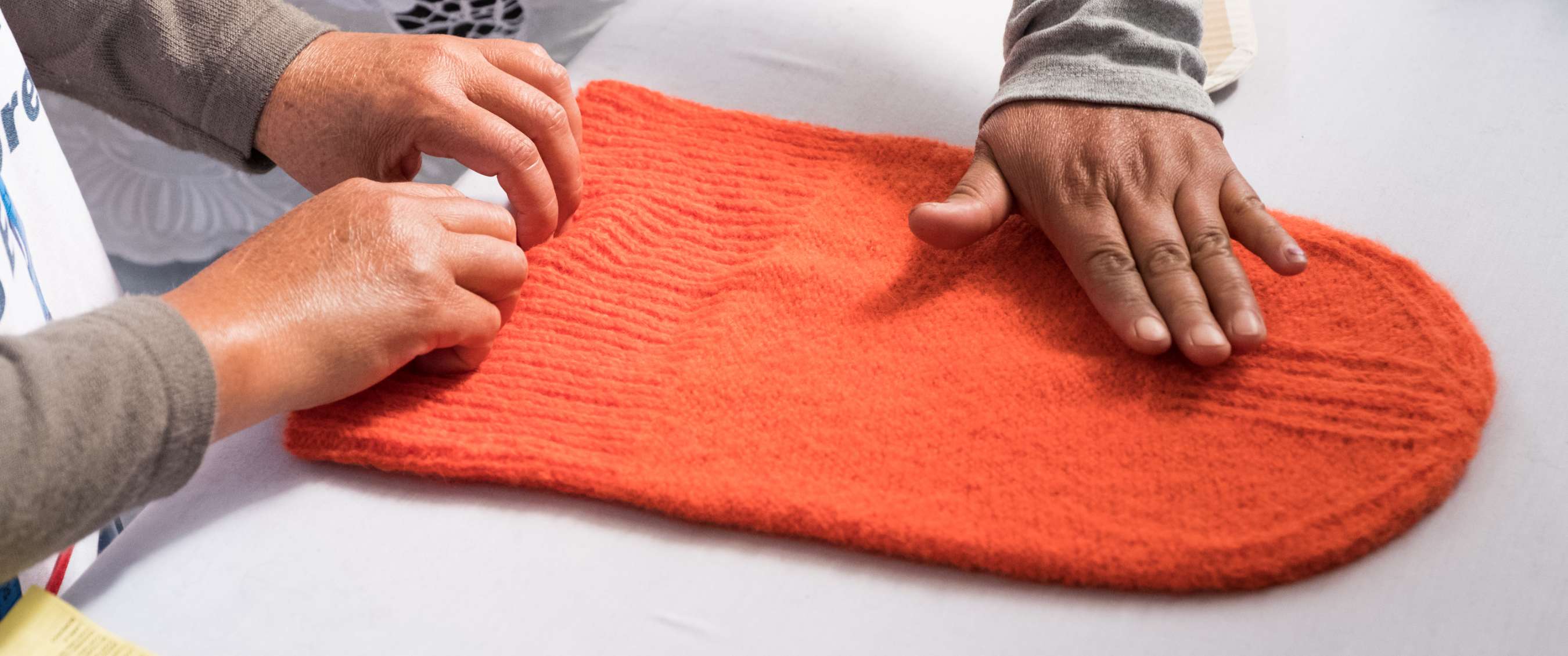 Deux paires de mains examinent un vêtement tricoté orange vif posé sur une table.