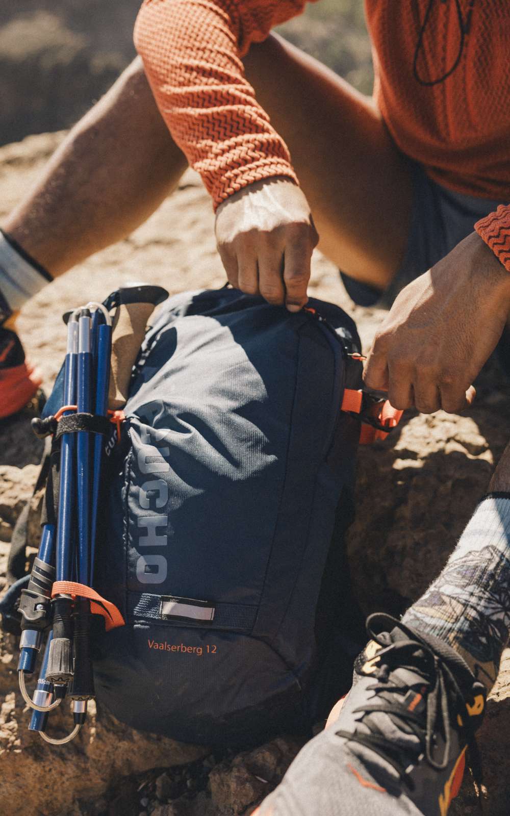 Des mains ferment un sac avec des bâtons de marche fixés sur le côté.