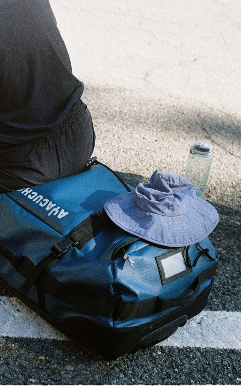 Sac de voyage bleu Ayacucho avec chapeau et gourde sur un sol ensoleillé