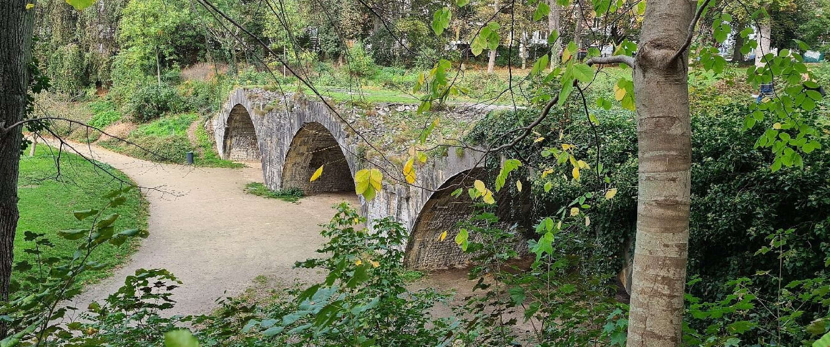 Pont en pierre à arches au-dessus d’un chemin dans un parc verdoyant à Namur.