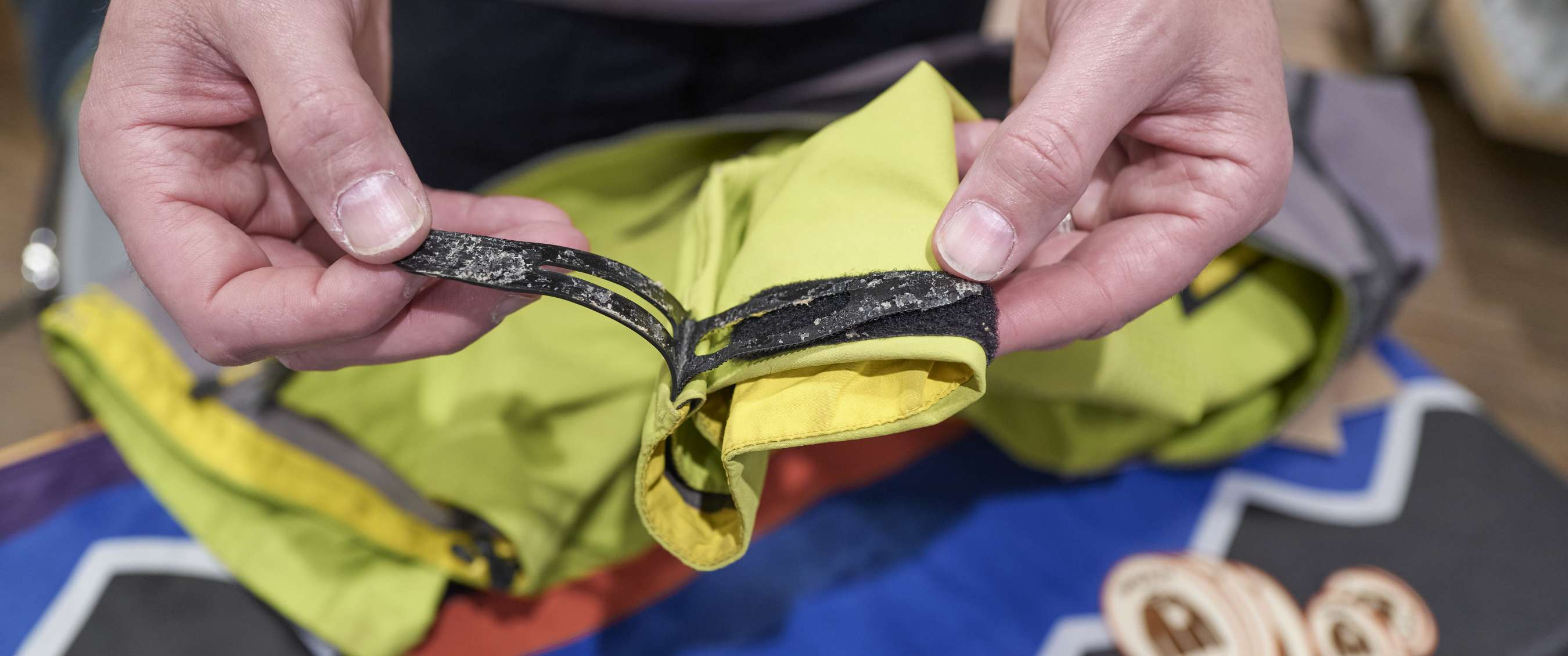 Gros plan sur des mains tenant une boucle usée sur un vêtement vert.