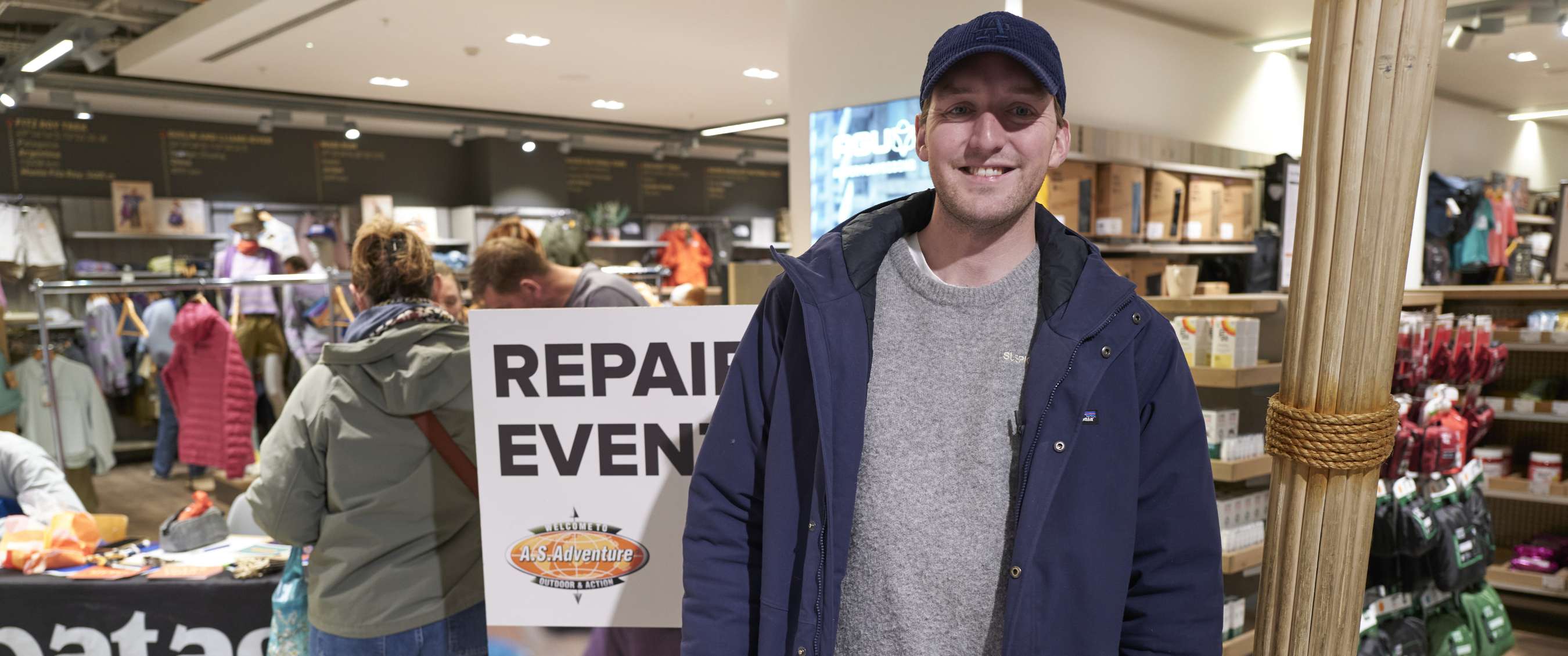Homme en veste bleue dans un magasin devant un panneau portant le texte REPAIR EVENT.