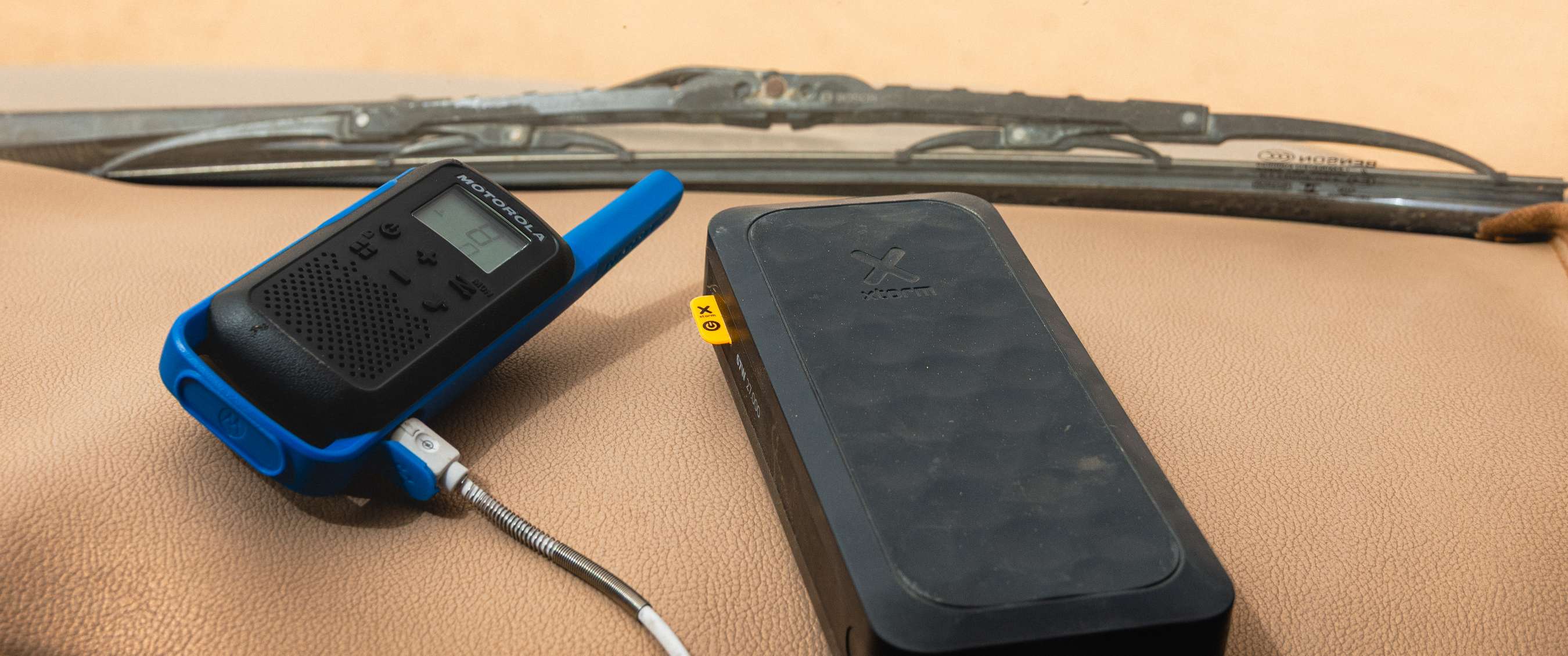 Walkie-talkie and Xstorm power bank on a dashboard with a windshield wiper in the background.