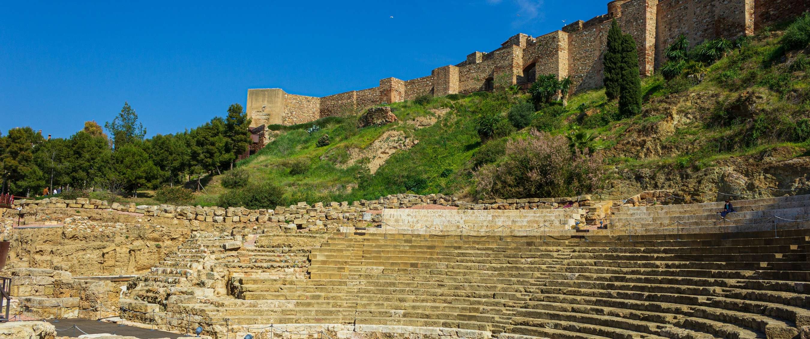 Théâtre romain avec gradins en pierre et remparts sur une colline verdoyante à Málaga.