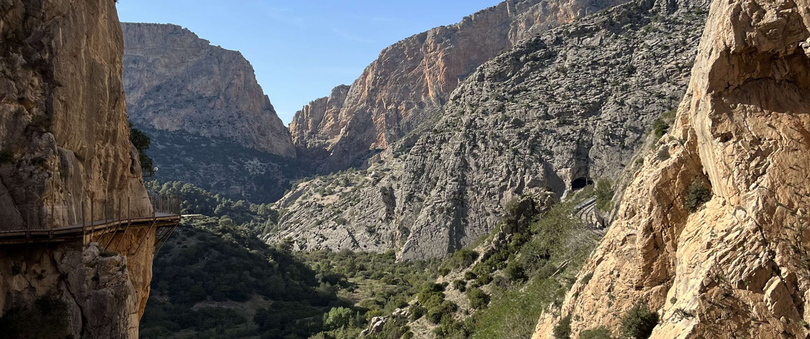 Sentier étroit le long de falaises abruptes dans une gorge verdoyante sous un ciel bleu.