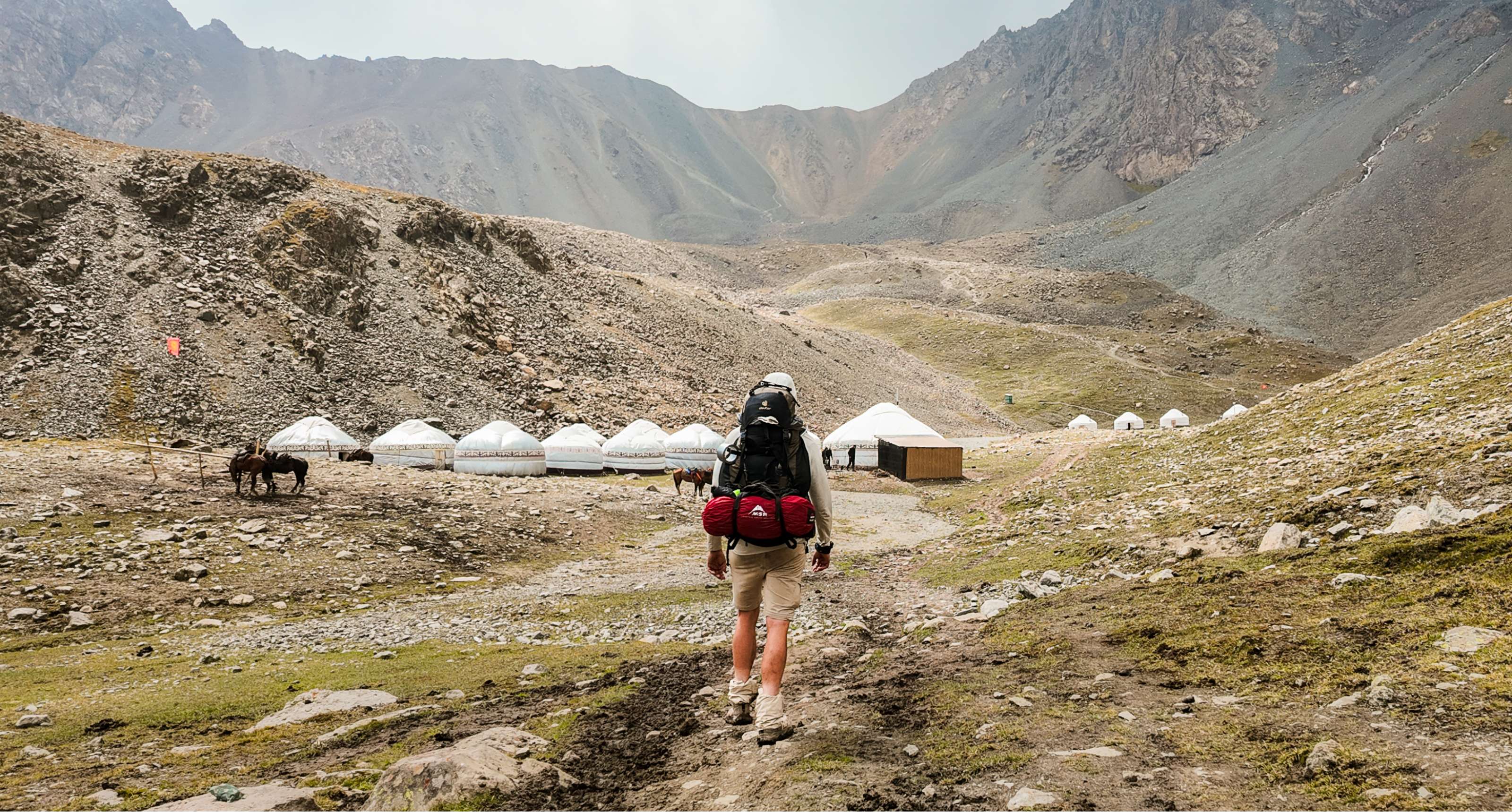 Randonneur avec sac à dos marche vers des yourtes blanches dans un camp de montagne isolé.