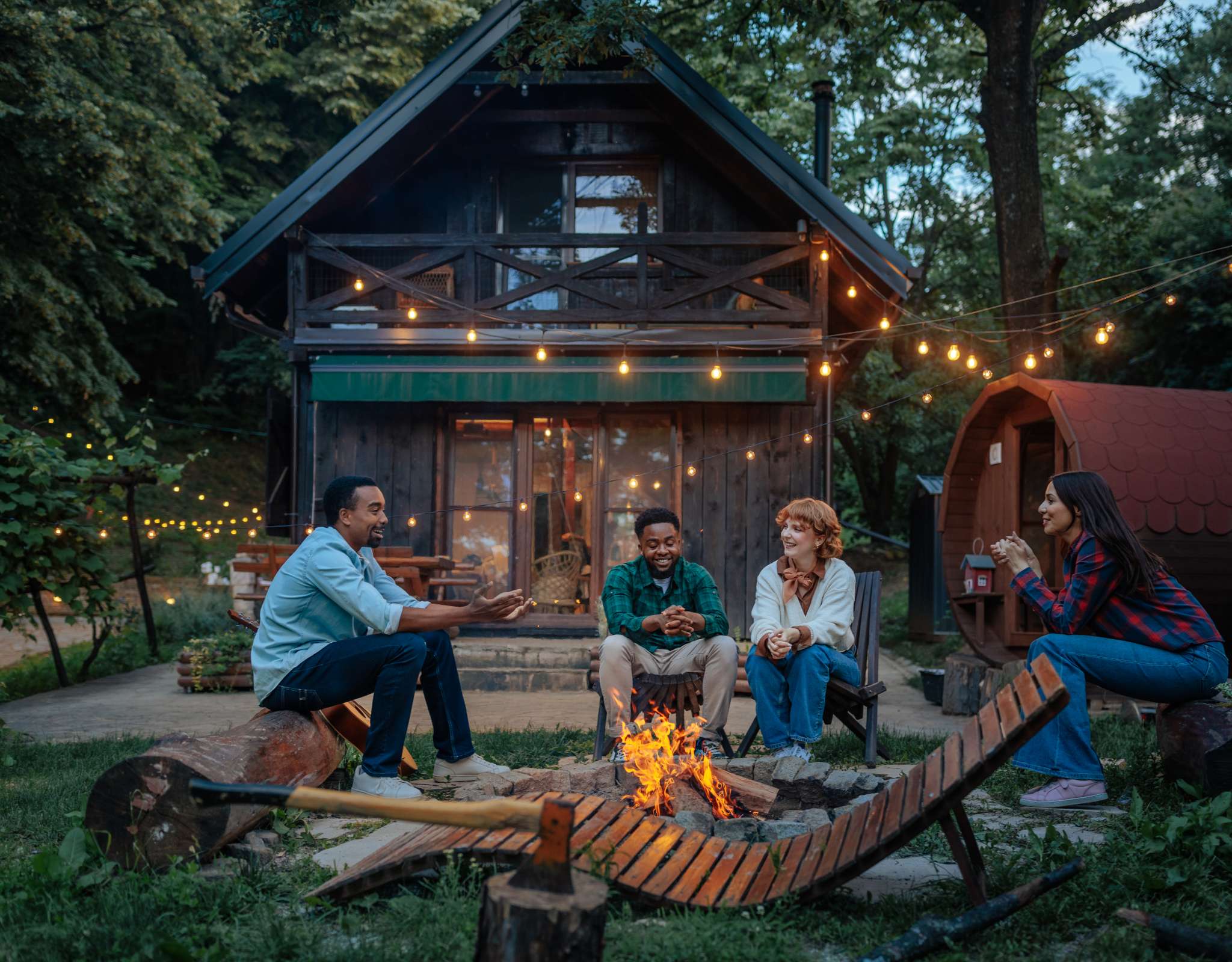 Quatre personnes assises autour d’un feu devant une cabane éclairée.