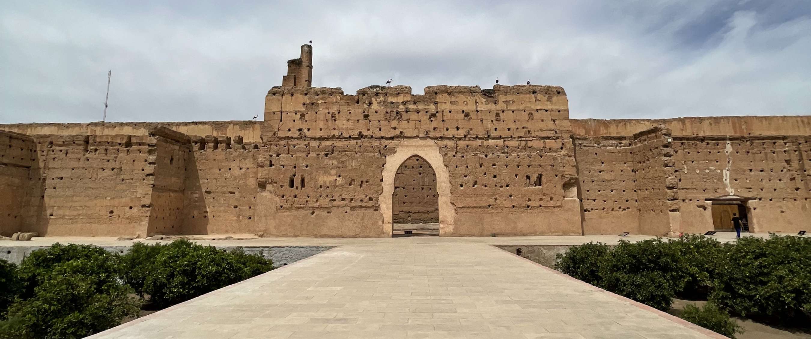 Grande muraille historique avec porte en arc au bout d’une large allée pavée.