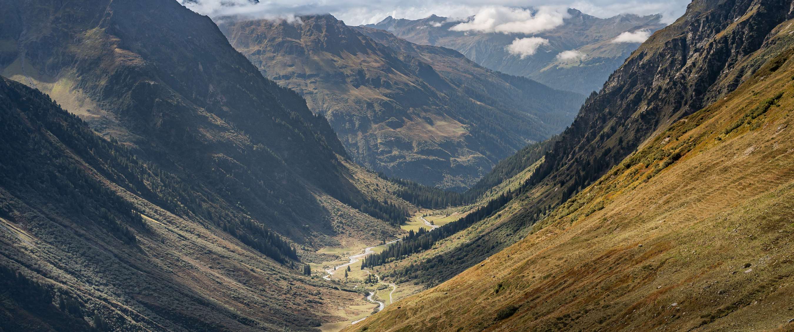 Vue sur une large vallée alpine avec une rivière sinueuse.