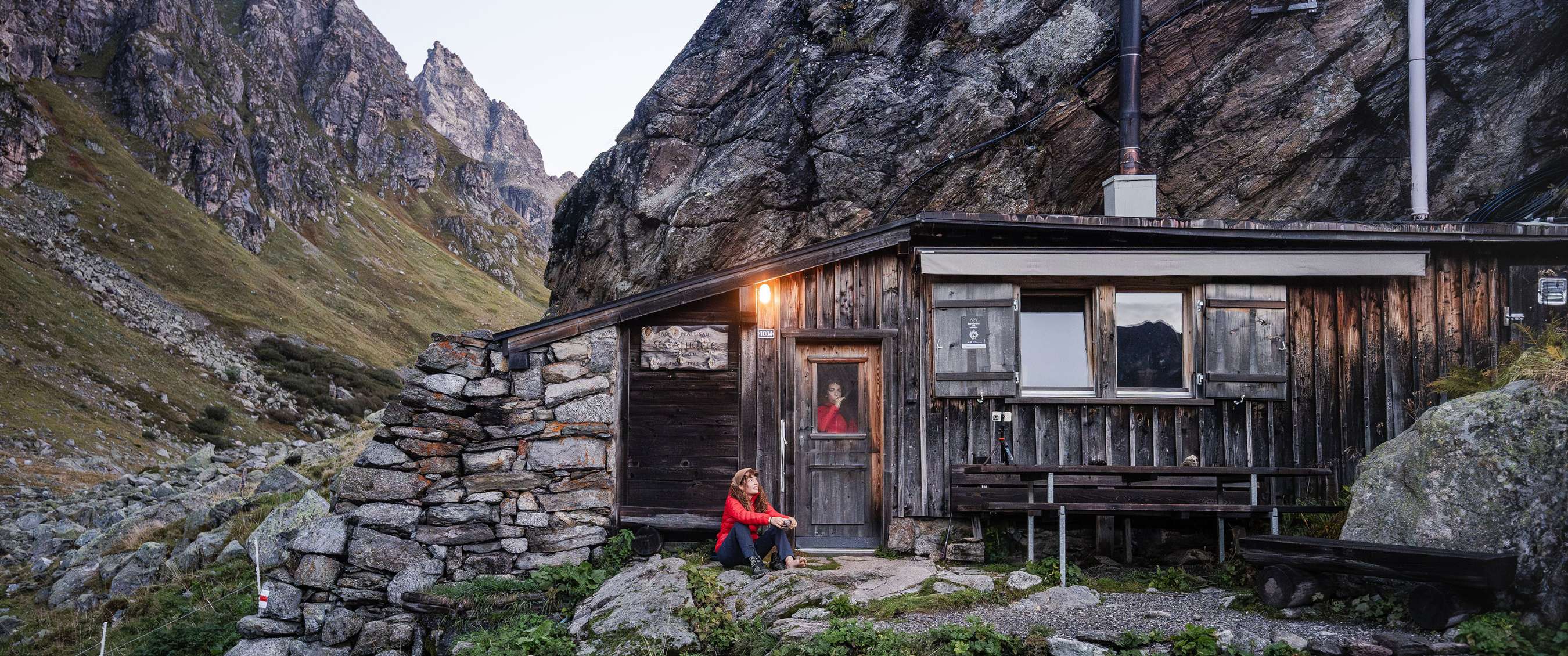 Personne assise devant un refuge dans un paysage montagneux rocheux.