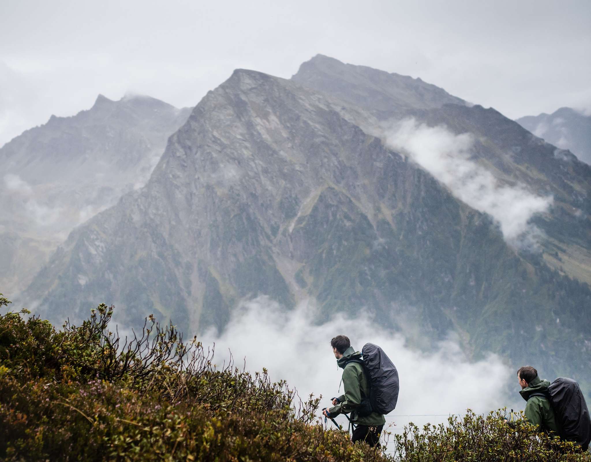 Deux personnes avec bâtons de marche en terrain alpin dans la brume.