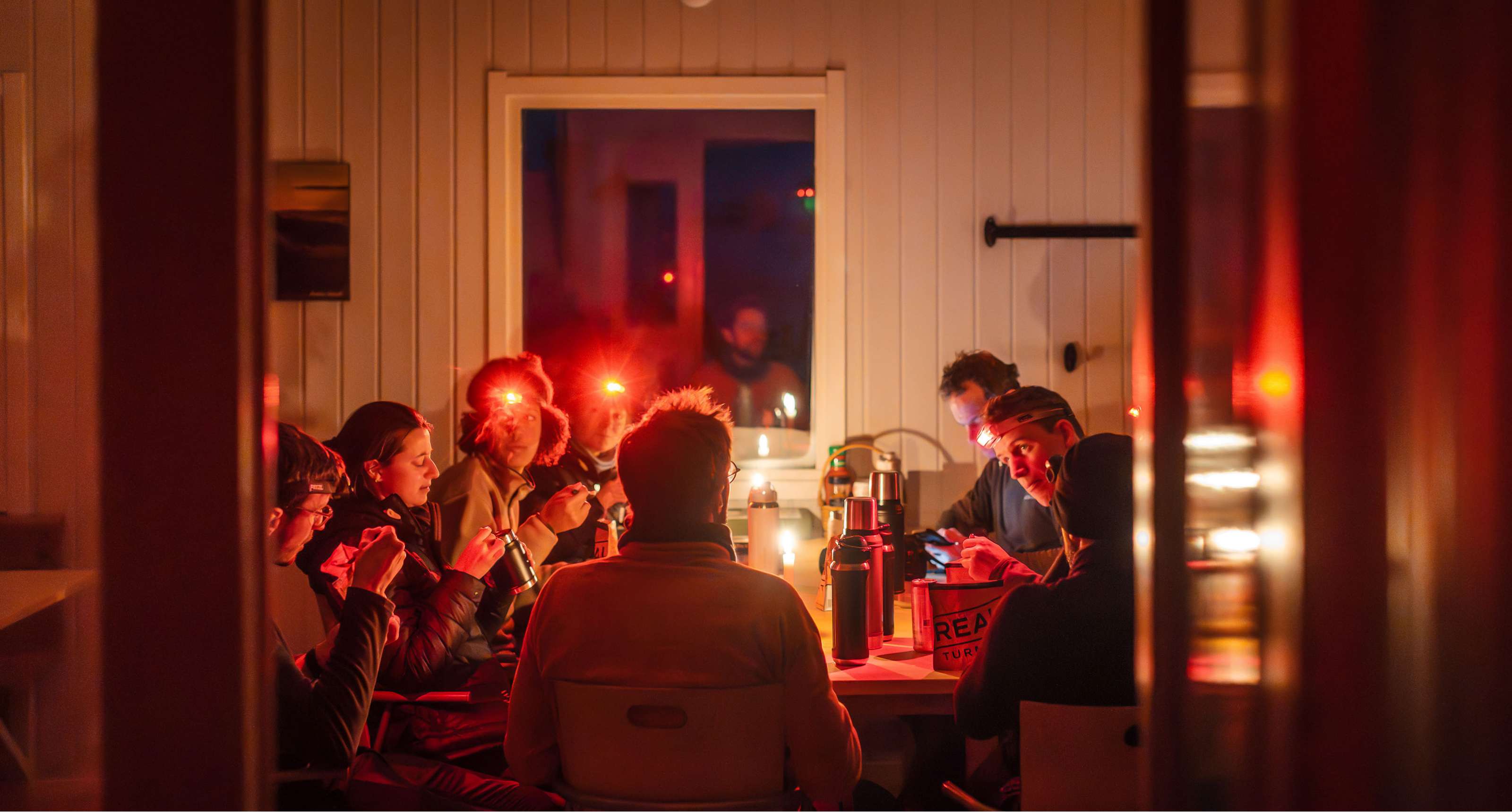 Groupe de personnes avec lampes frontales mange autour d’une table dans une pièce en bois éclairée.