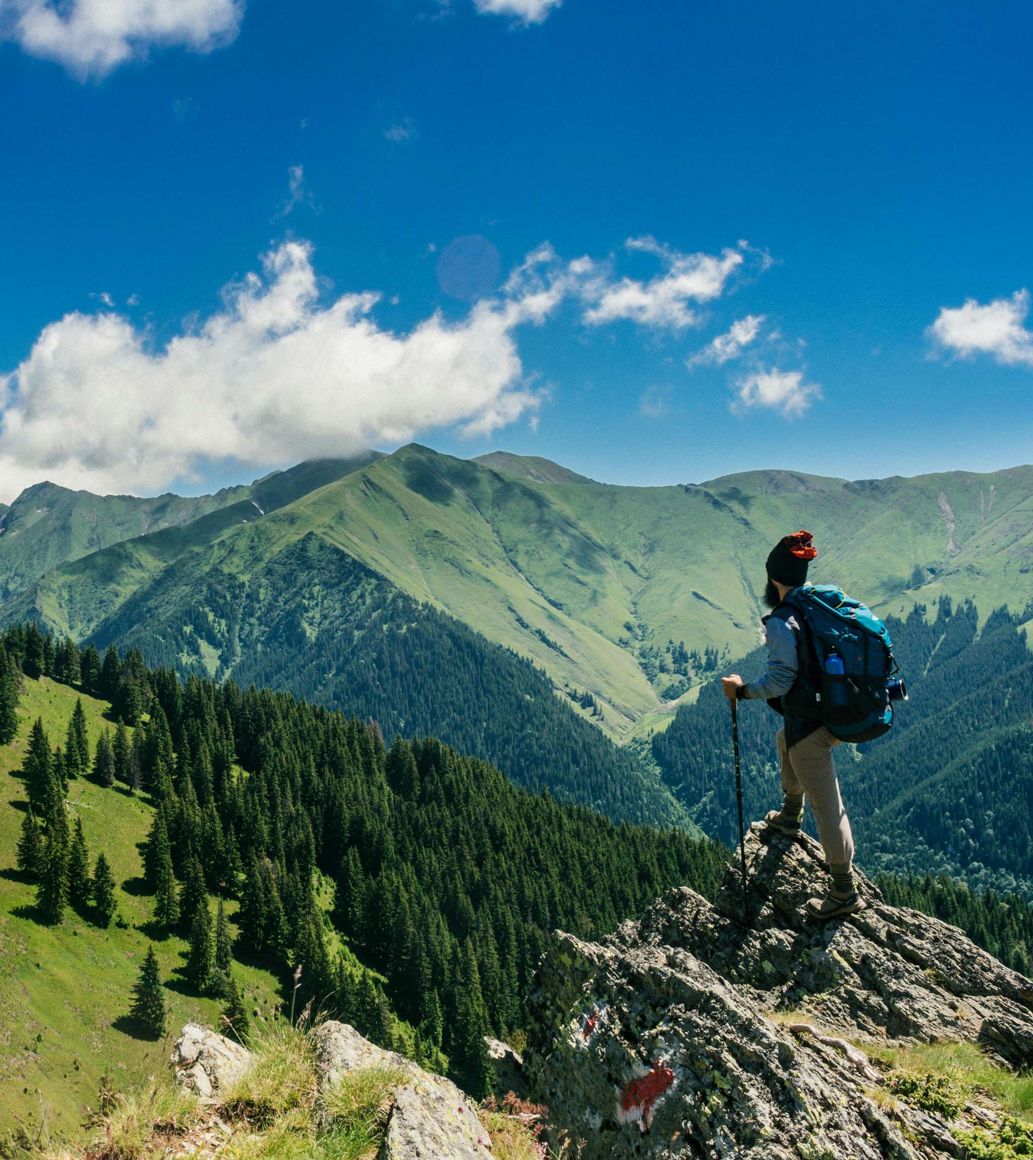 Personne équipée de randonnée sur une crête avec des collines boisées en arrière-plan.