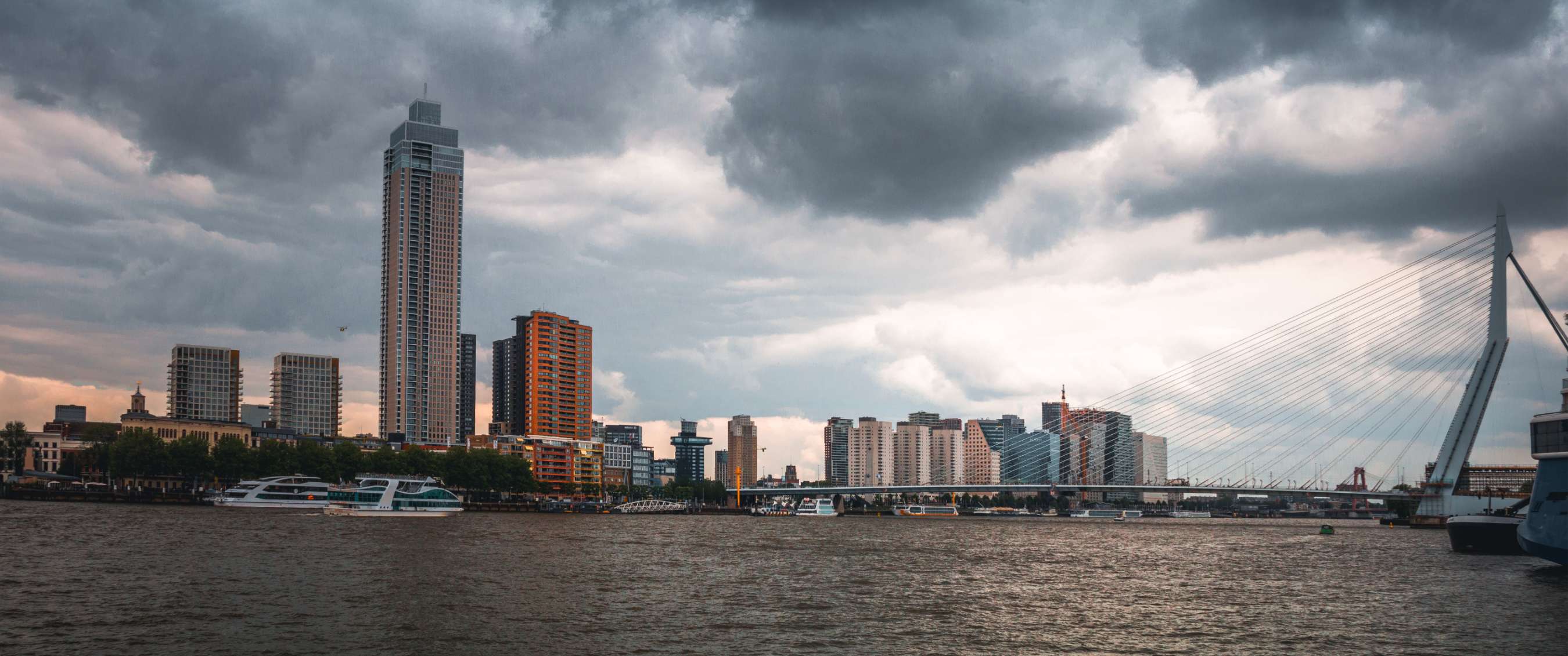 Skyline urbaine au bord d’une rivière sous des nuages sombres.