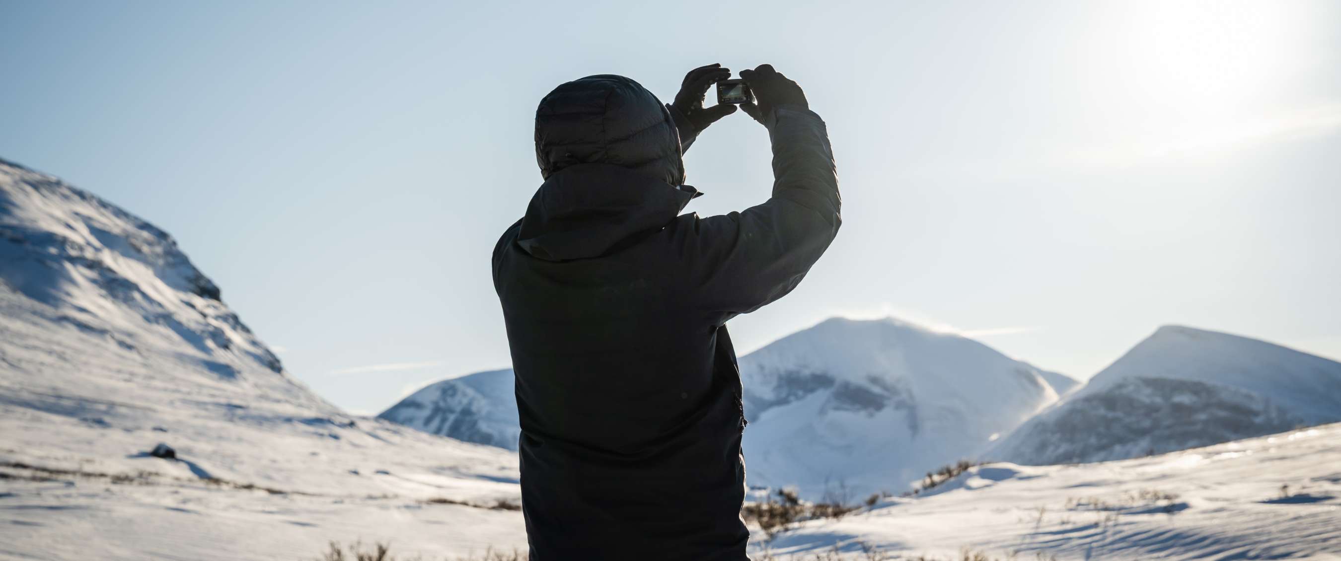 Personne photographiant des montagnes enneigées avec une petite caméra à la main