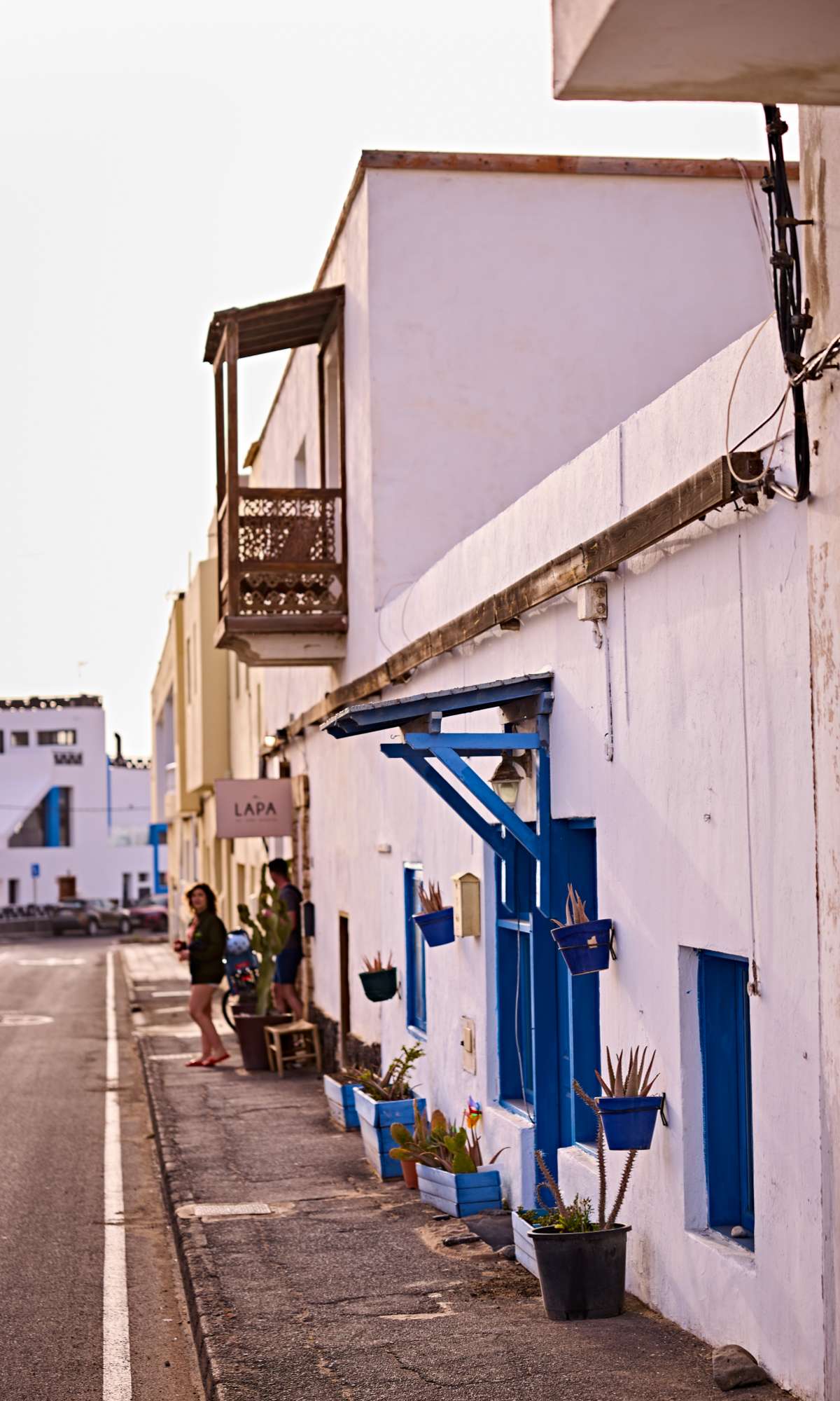 Façade blanche avec fenêtres bleues et pots de fleurs le long d’une rue calme.