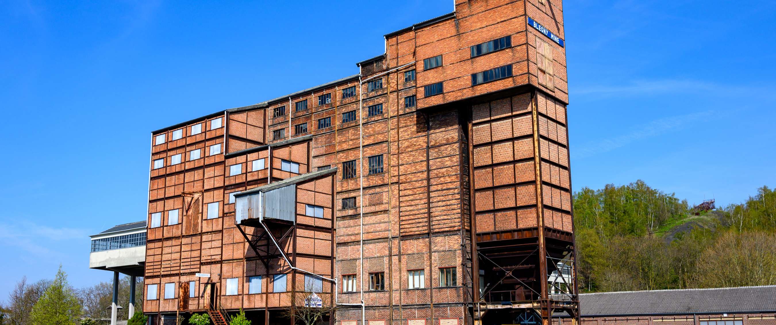 Grand bâtiment minier historique en briques avec structures métalliques et plusieurs étages.