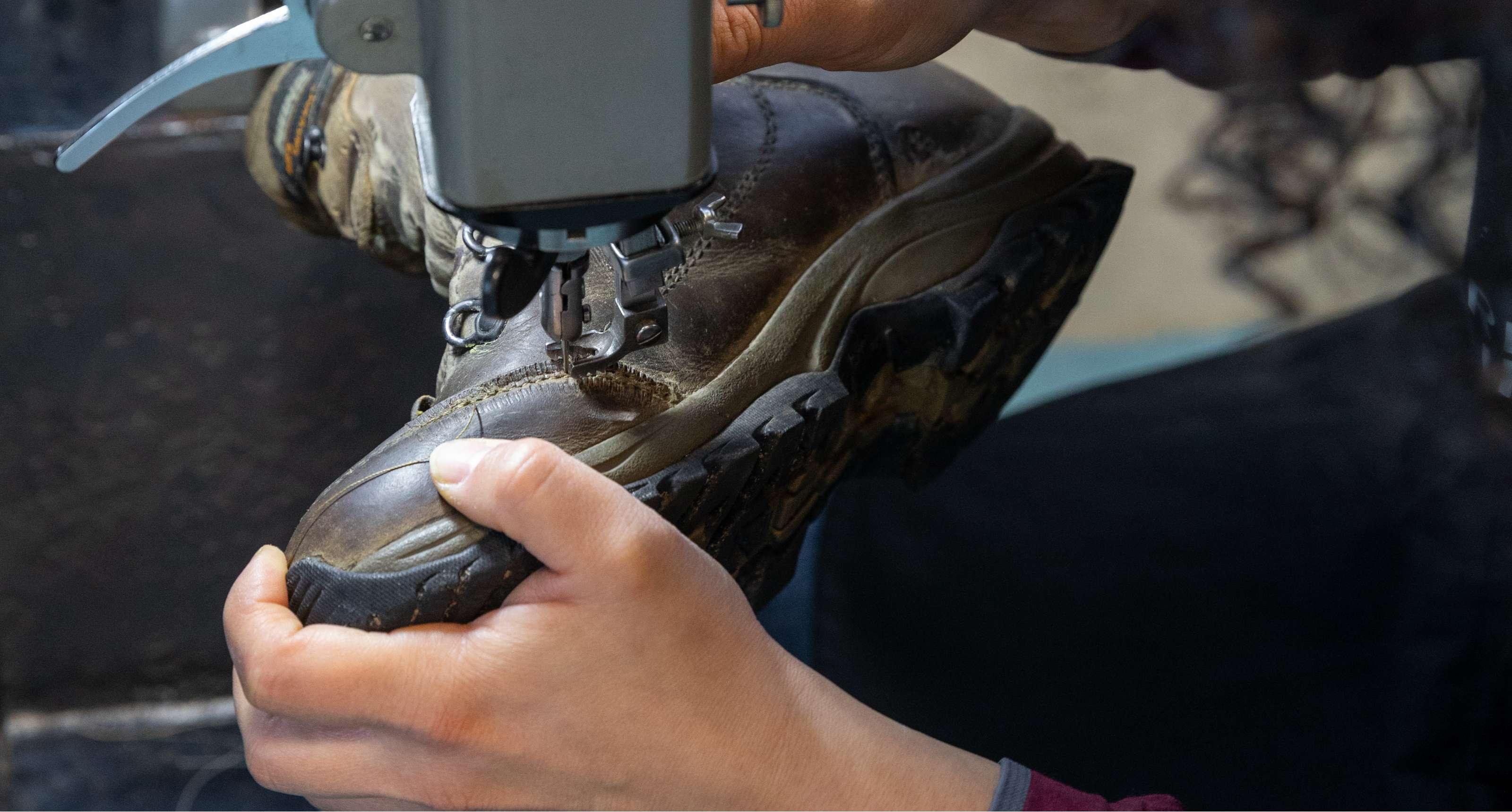 Un cordonnier recoud une couture d'une chaussure de randonnée en cuir avec une machine à coudre.