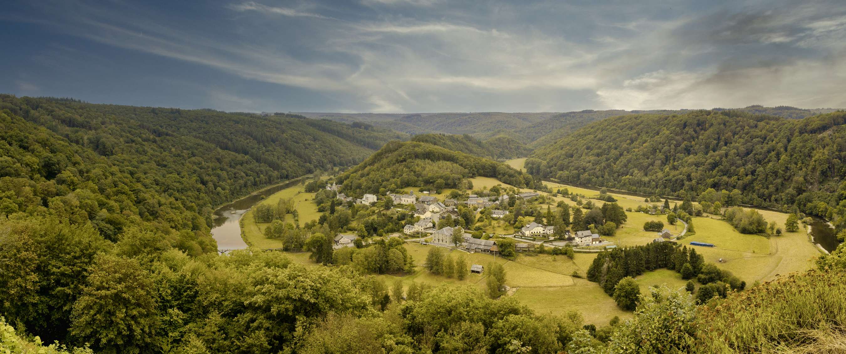 Vue panoramique sur un village, une rivière et des collines boisées dans une vallée verte