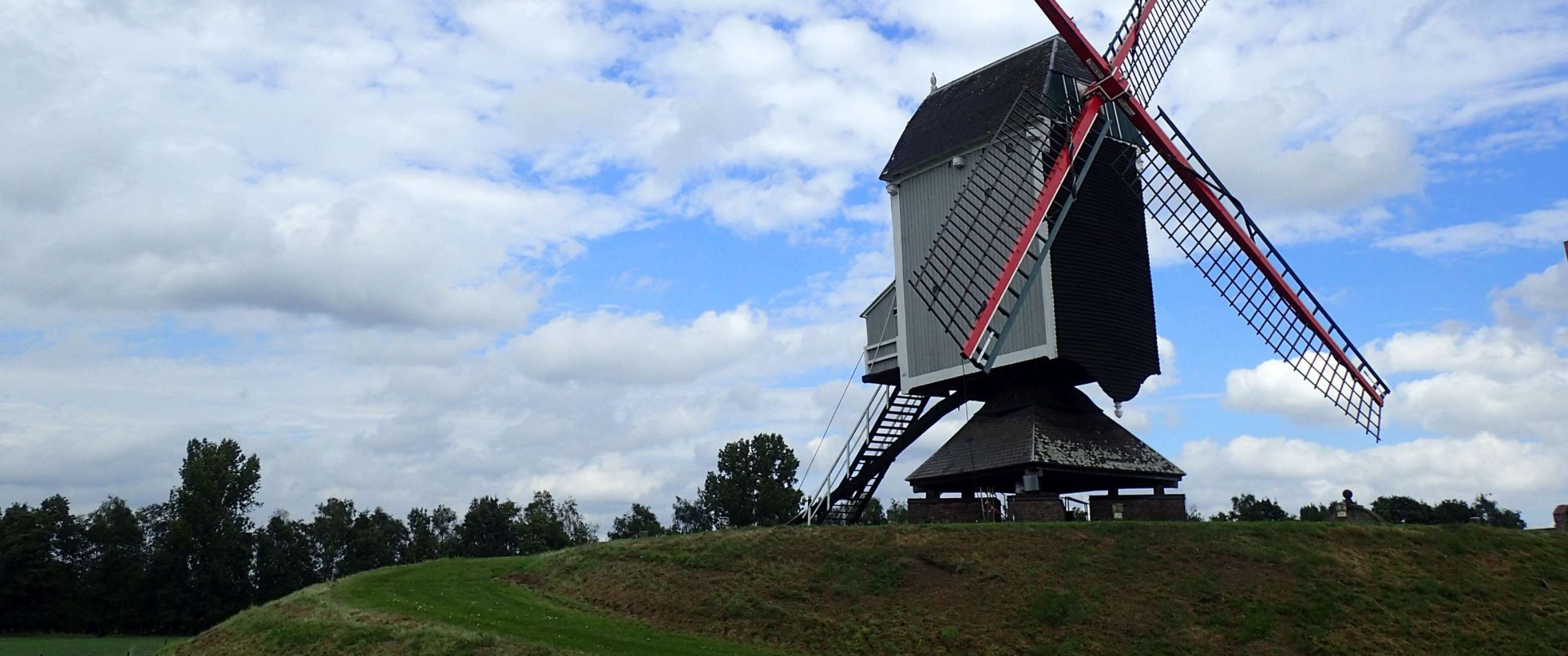 Moulin à vent traditionnel sur une colline verdoyante sous un ciel partiellement nuageux.