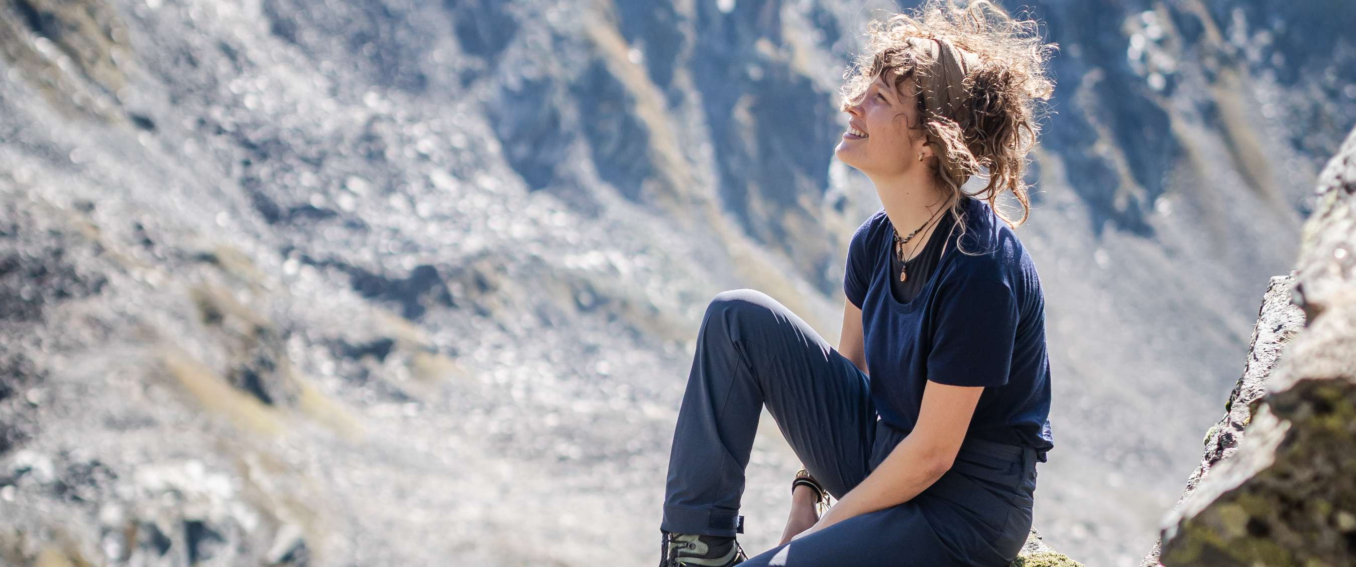 Personne en tenue de randonnée se repose sur une pente rocheuse en montagne.