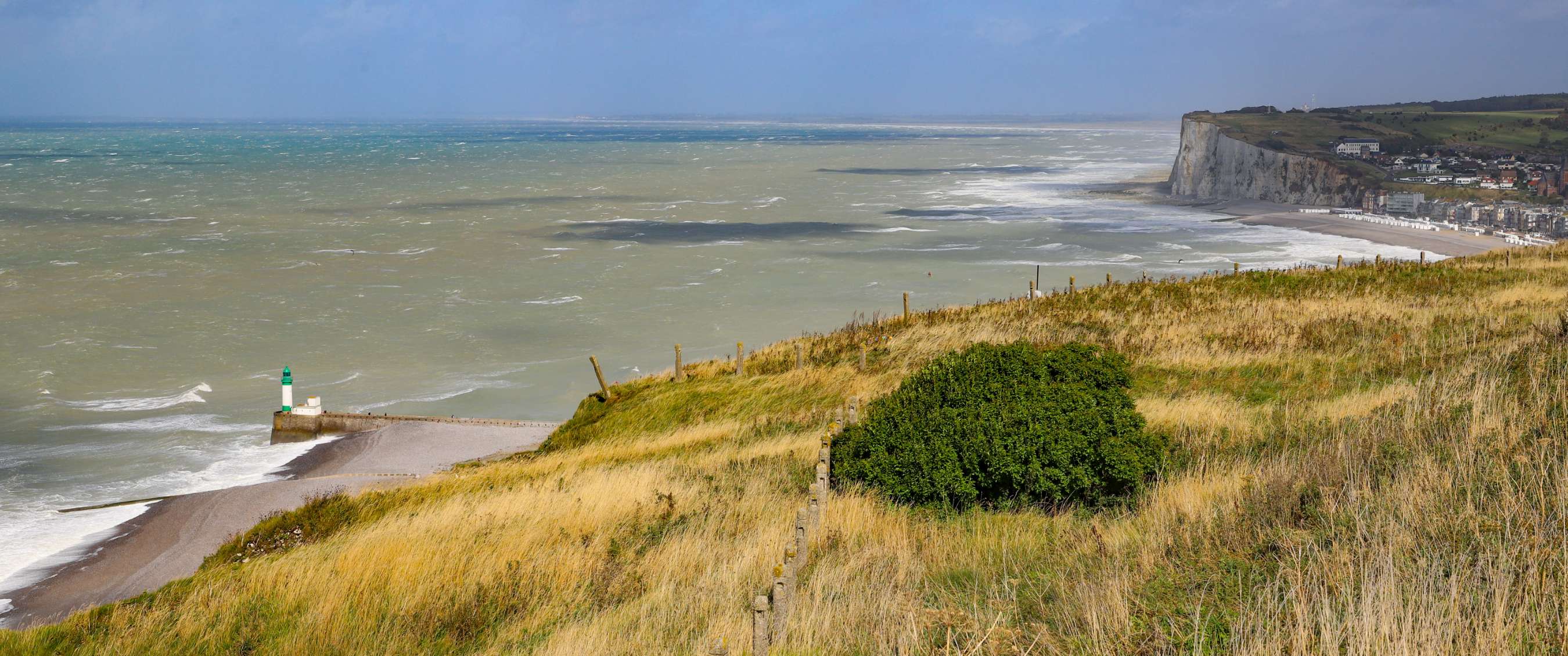 Côte herbeuse dominant la mer et de hautes falaises blanches sous un ciel bleu nuageux.