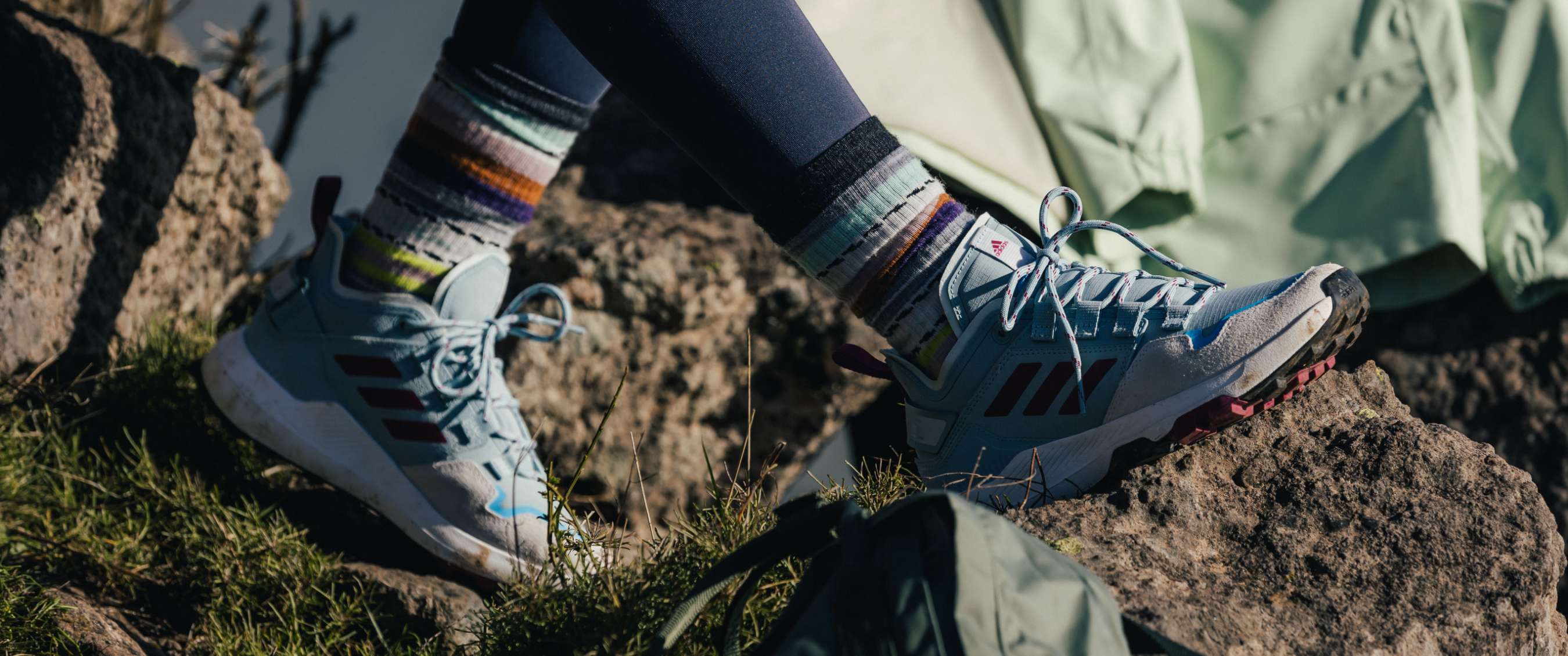 Gros plan de chaussures de randonnée avec chaussettes rayées sur un sol rocheux.