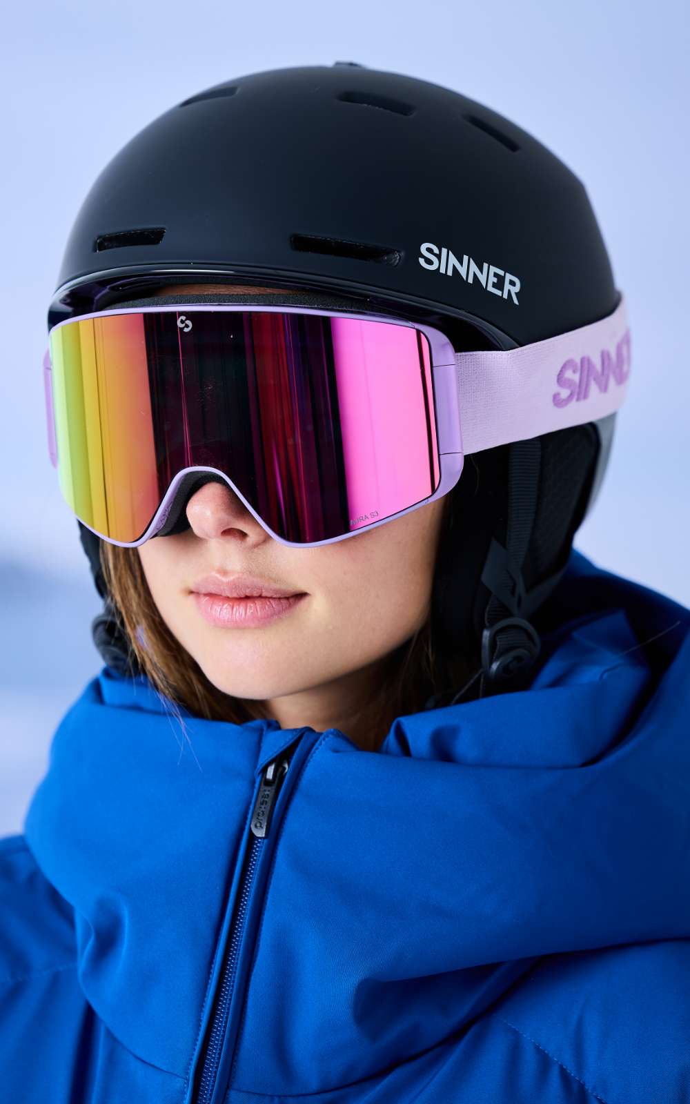 Gros plan d'une femme avec un masque de ski Sinner à écran miroir rose et un casque noir.
