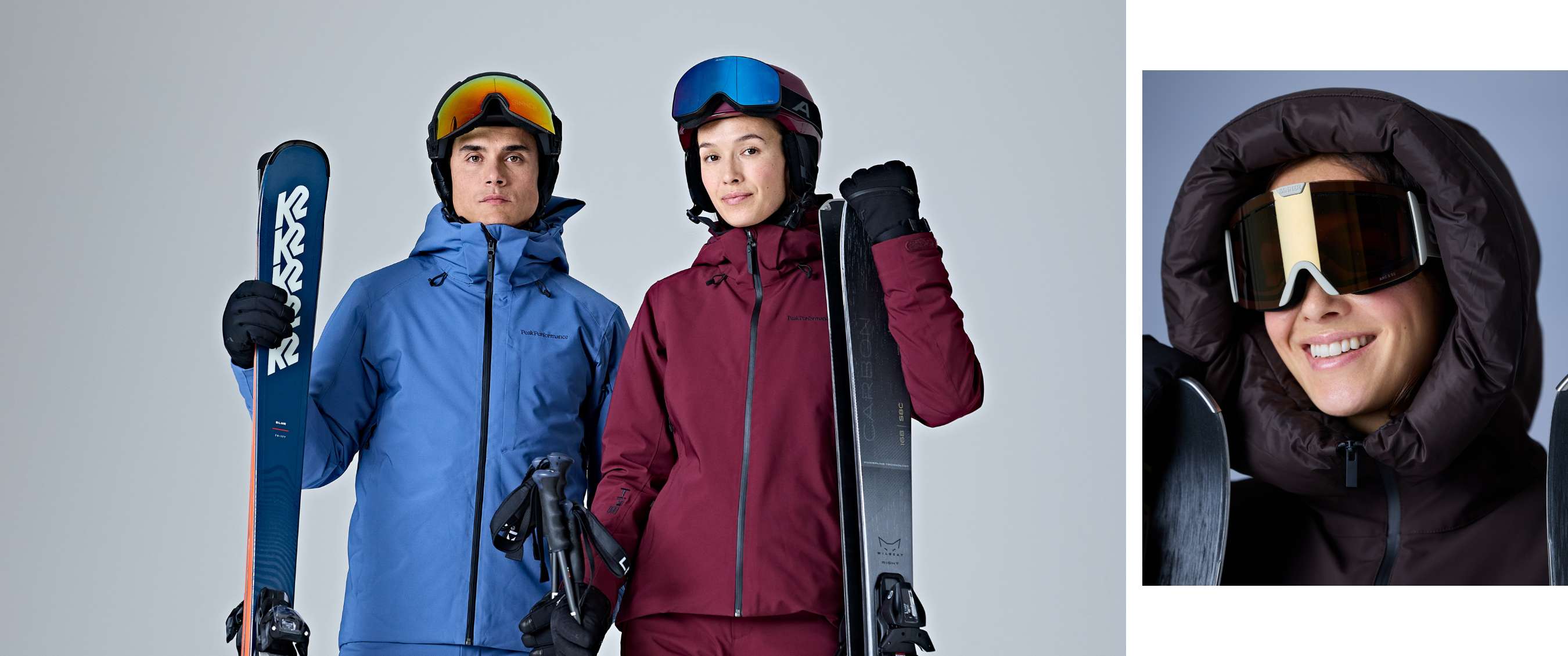Deux skieurs en tenues bleue et bordeaux posent avec des skis et leurs masques sur leurs casques.