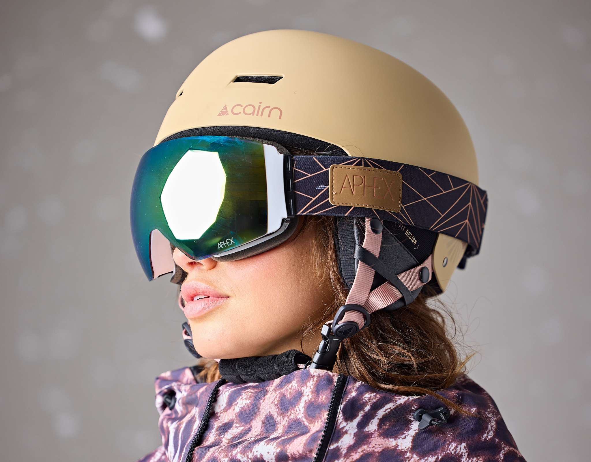 Personne en tenue de ski, penchée vers l’avant, portant un casque de ski vert et un masque bleu sur fond neutre.