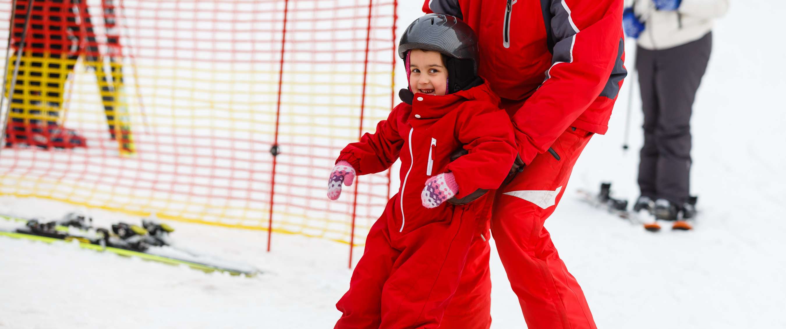 Enfant souriant en combinaison rouge soutenu sur la piste.