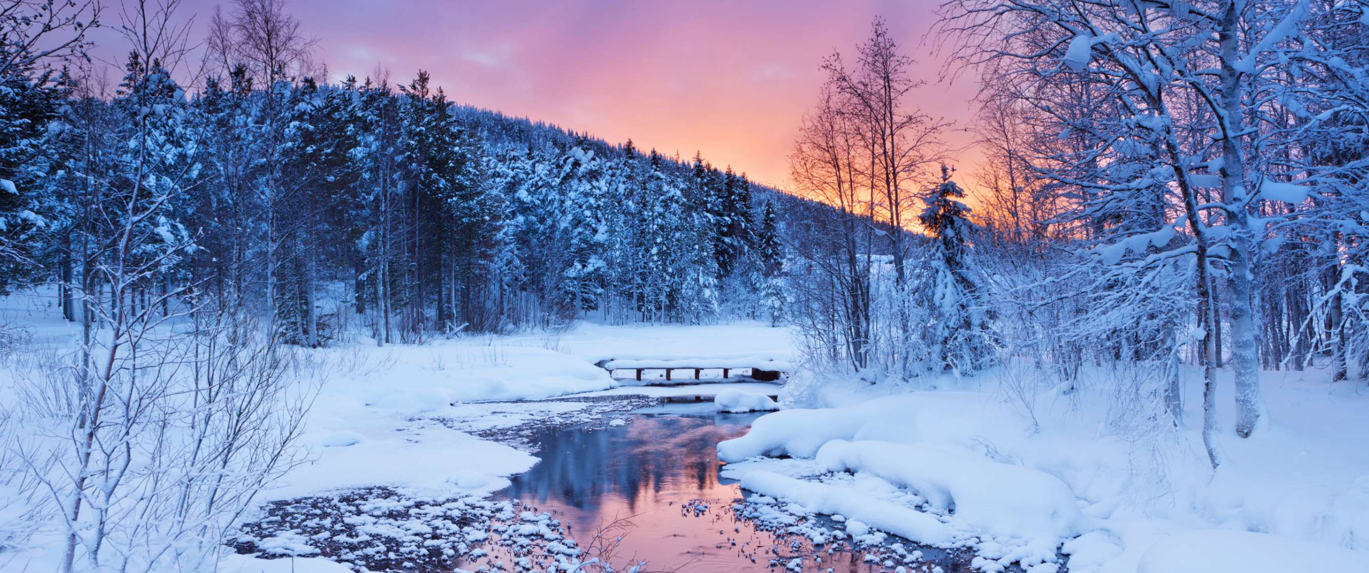 Forêt enneigée avec rivière gelée sous lever de soleil rosé.
