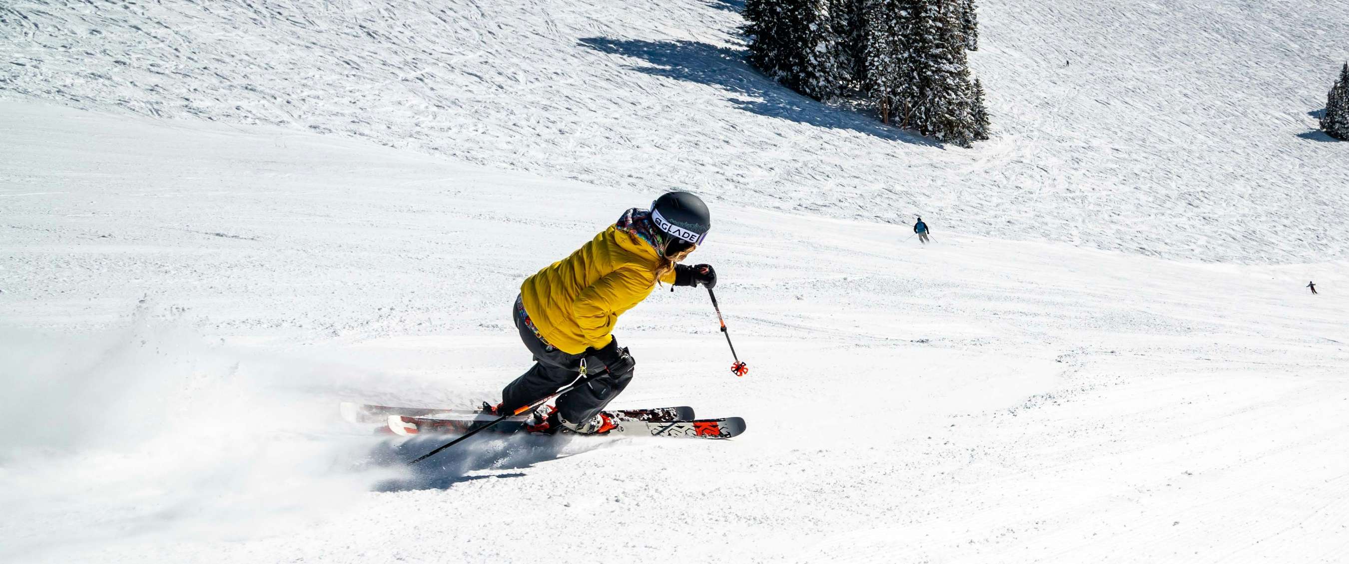 Une personne à skis en veste jaune et gants noirs prend un virage sur une piste enneigée.