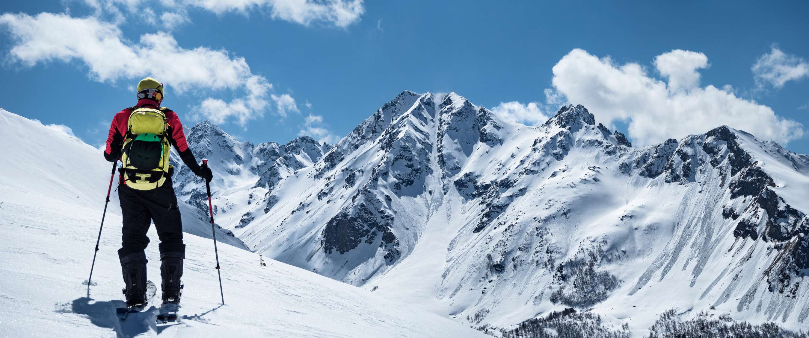 Un skieur observe la chaîne de montagnes enneigées sous un ciel bleu clair.
