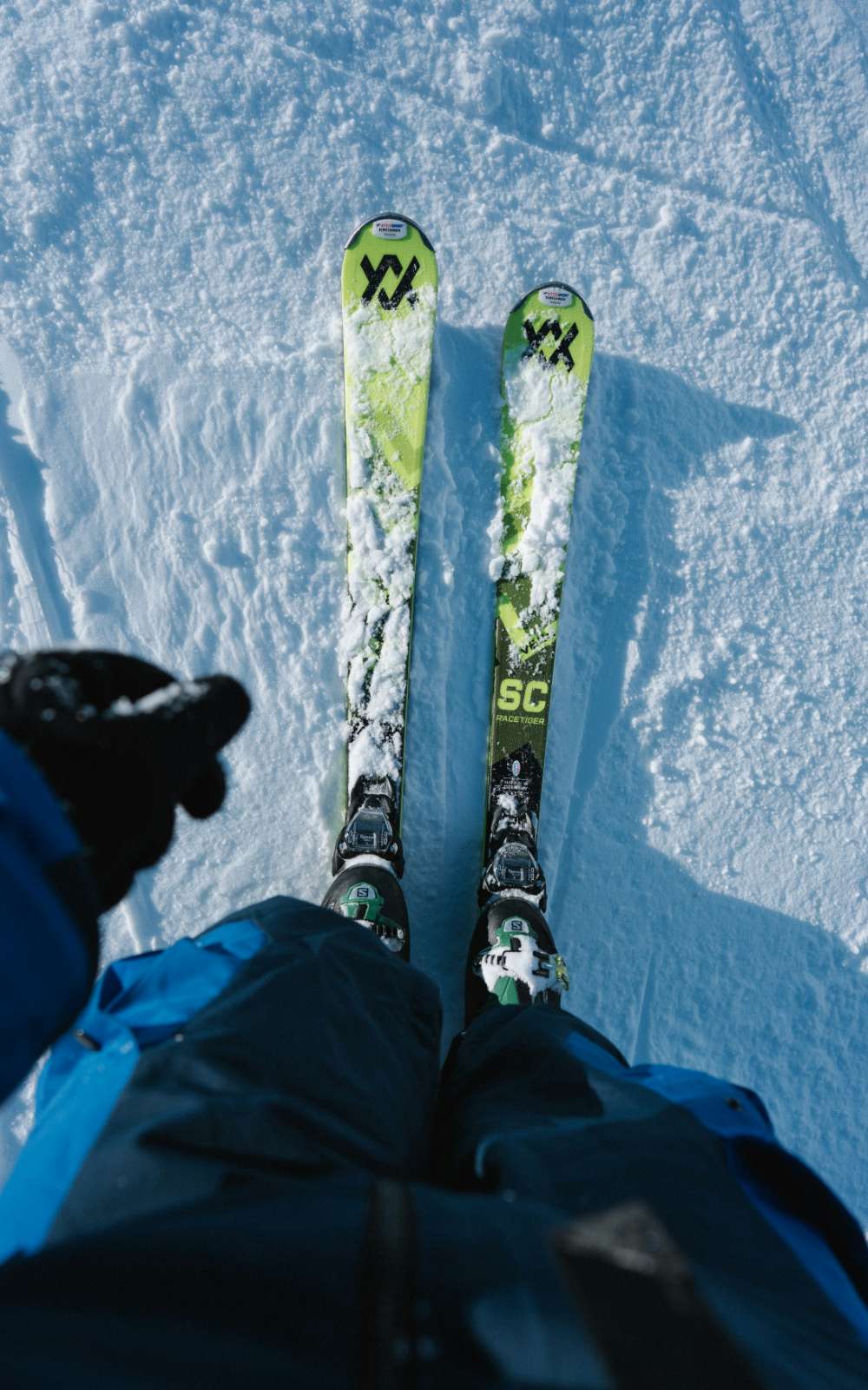 Vue de dessus de deux skis verts couverts de neige et de chaussures enclenchées dans les fixations.