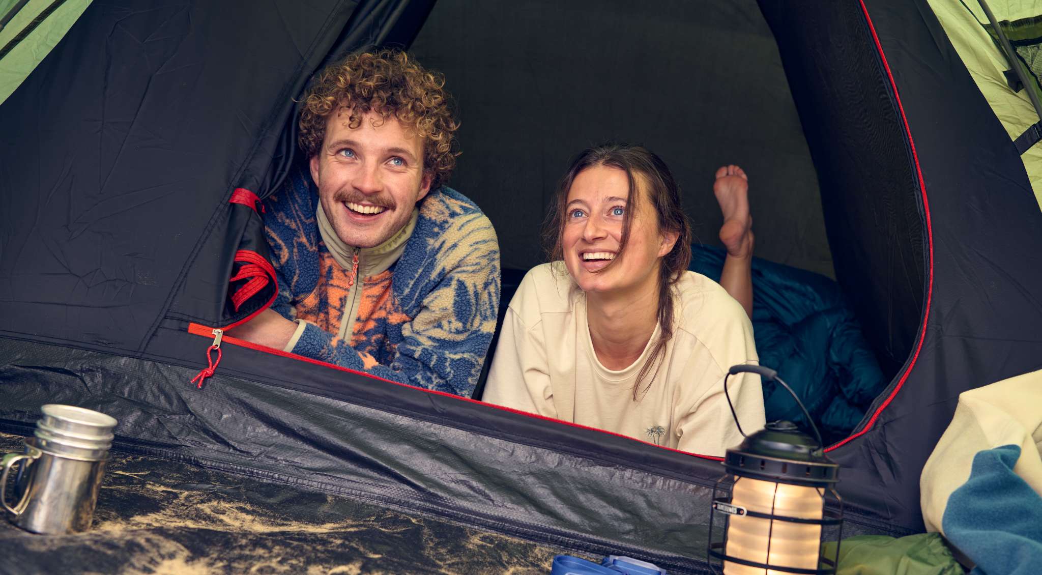 Deux campeurs souriants sont allongés à l’entrée d’une tente