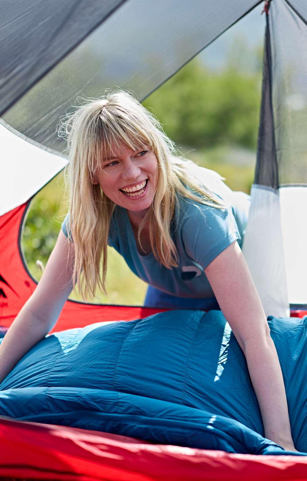 Femme souriante assise dans un sac de couchage bleu dans une tente rouge