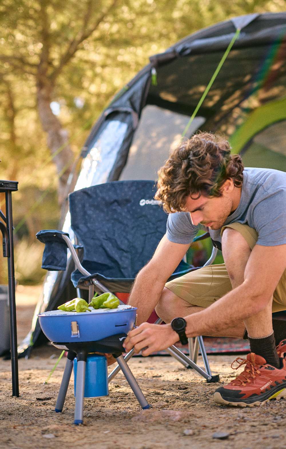 Homme réglant un petit barbecue sur un camping à côté d’une tente