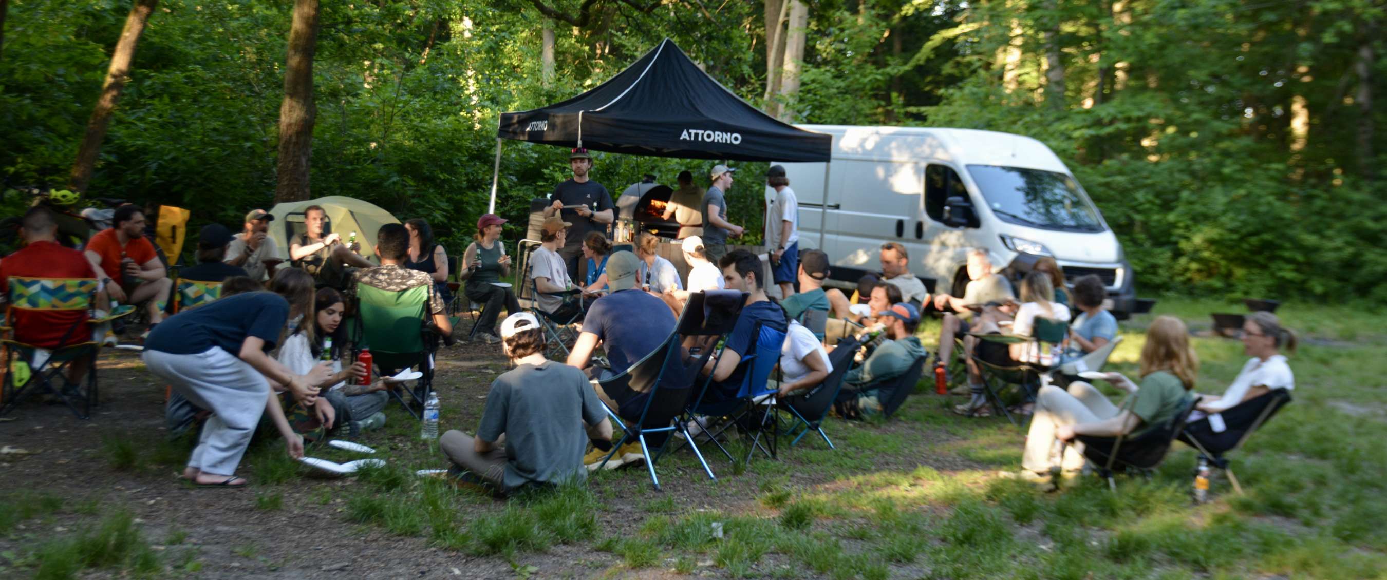 Groupe de personnes assises près d’une tente noire ATTORNO dans la forêt.